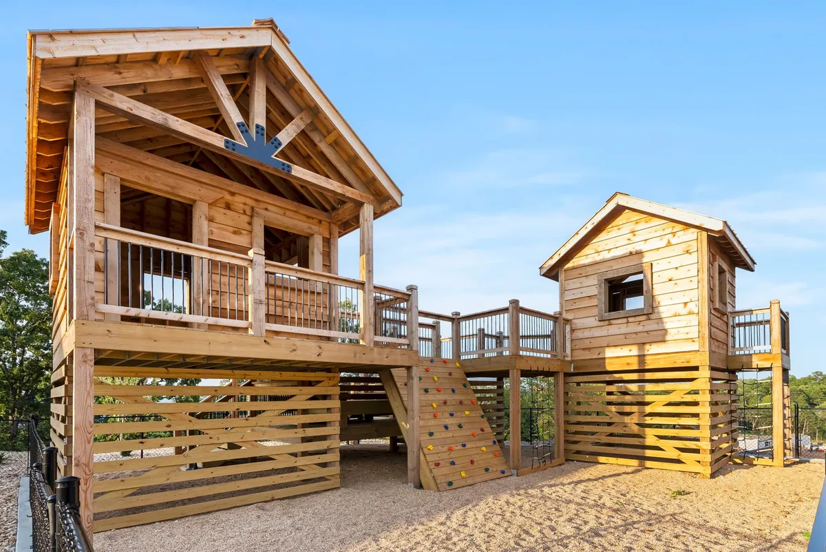 A whimsical treehouse playground complete with a slide, stairs, and a small adjacent playhouse, inviting children to climb, play, and spark their imaginations. The structure is set amidst a safe and sunny outdoor space.