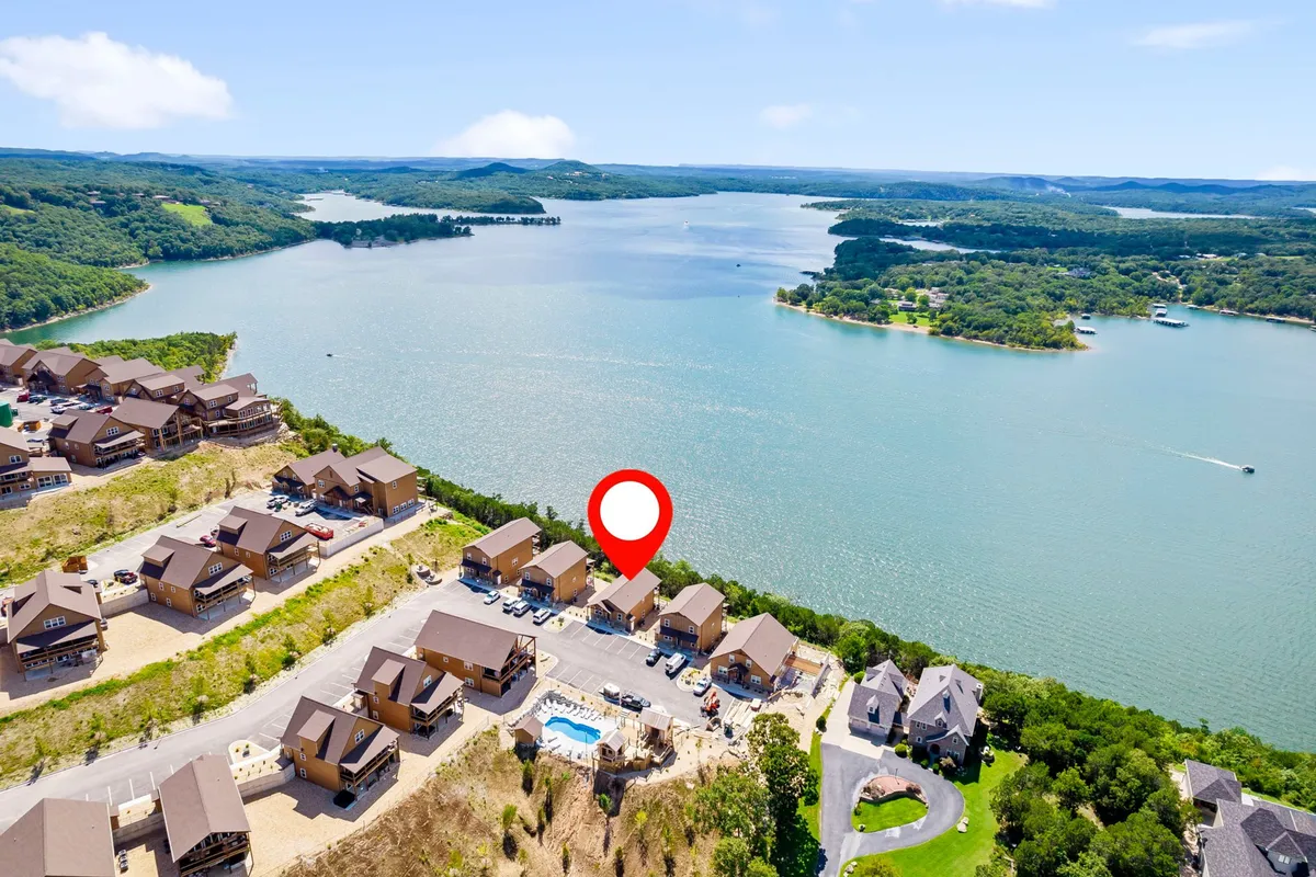 A panoramic view featuring a tranquil lake bordered by houses and a swimming pool, all surrounded by abundant greenery. The scene highlights the proximity of natural beauty and water-based amenities, providing a sense of peace and escape.