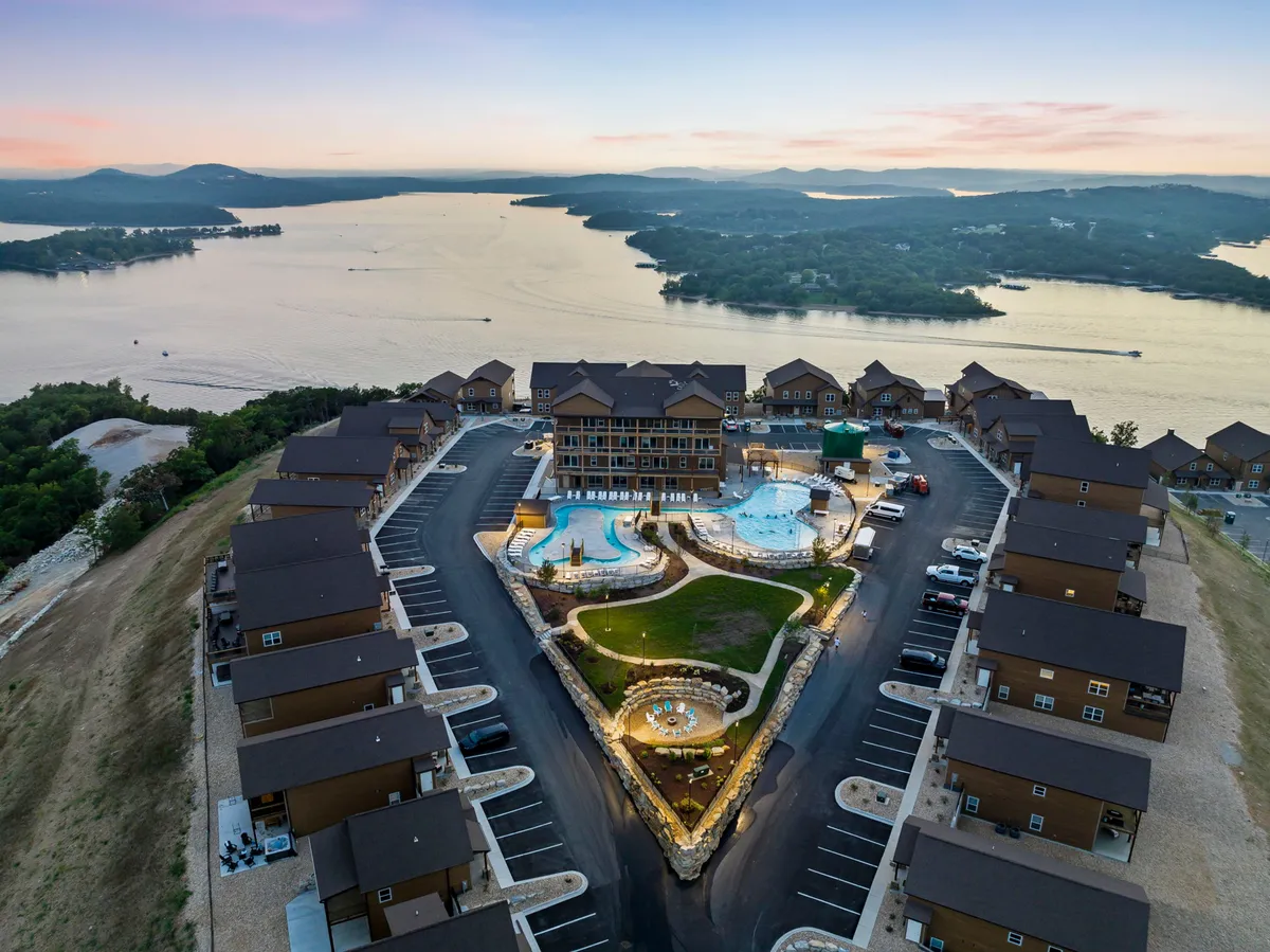An inviting exterior view of swimming pools surrounded by landscaped gardens, with the lake and modern architectural elements in the background. The setting is designed for both relaxation and social gatherings, capturing the lakeside leisure vibe.