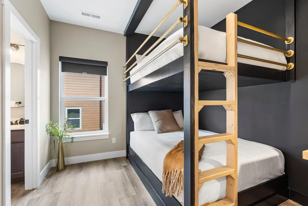 A playful, inviting bedroom with a large bunk bed, decorated throw, and a window letting in natural light. The space feels cozy and perfect for kids or families sharing a room.