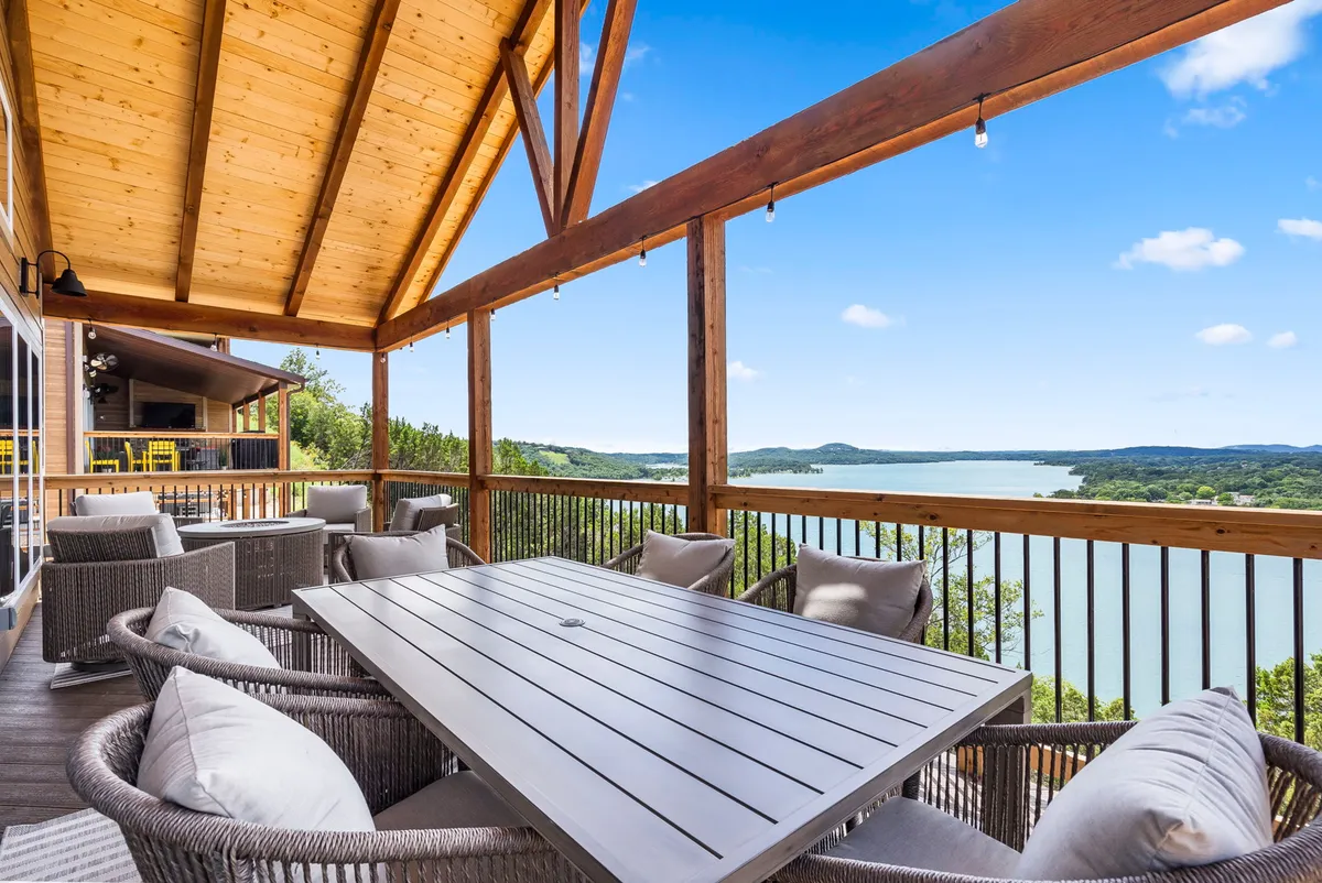 This image captures a serene exterior dining space featuring a wooden table, outdoor seating, and a breathtaking lake view framed by sturdy wooden beams. The scene is inviting, set up for enjoying meals or drinks with the beauty of nature all around.