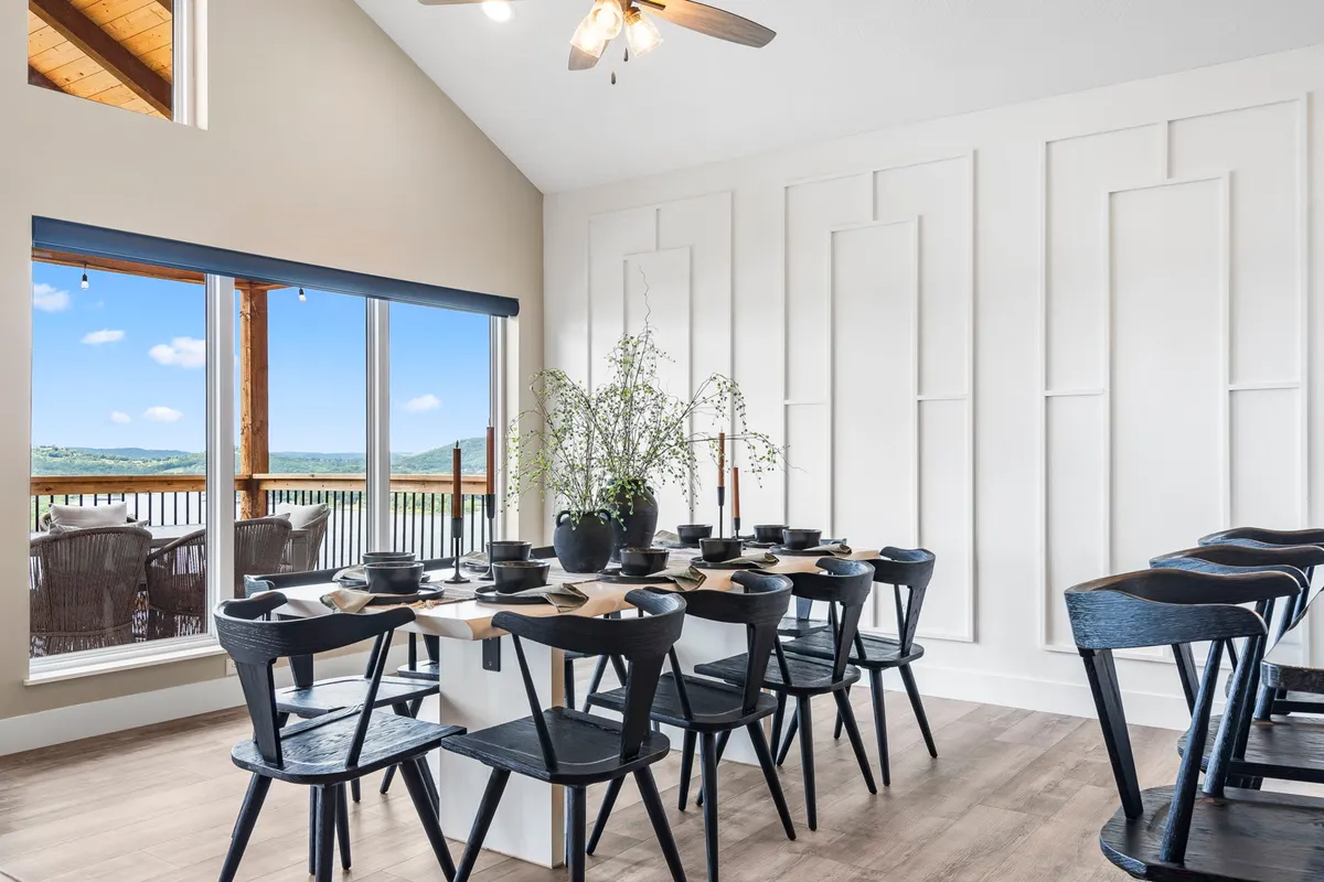 A spacious dining table is set near large windows, allowing for abundant natural light and views of the outdoors. The table is adorned with a decorative vase, creating a warm and welcoming setting for group meals.