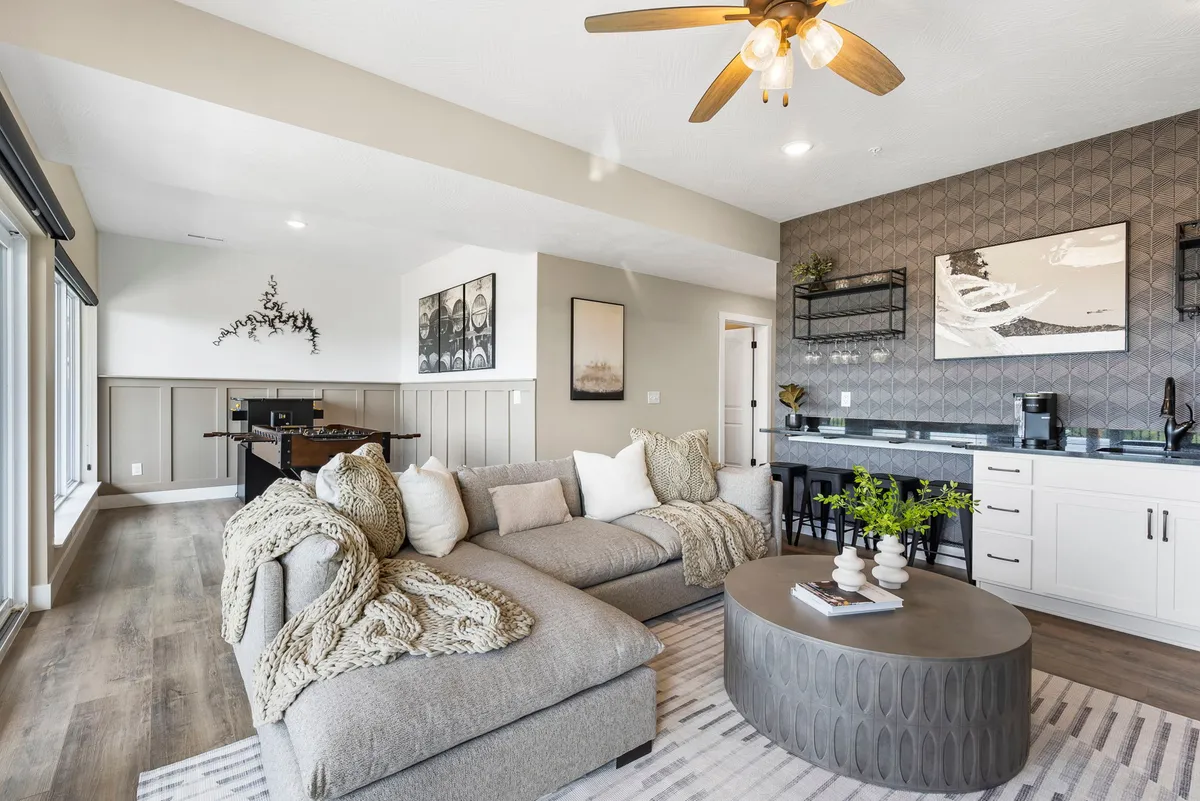 Another perspective on a stylish entertainment lounge featuring a large sectional sofa, a round coffee table, and a kitchenette area in the background. Decorative art and soft lighting add warmth and comfort to the scene, inviting guests to relax or entertain.