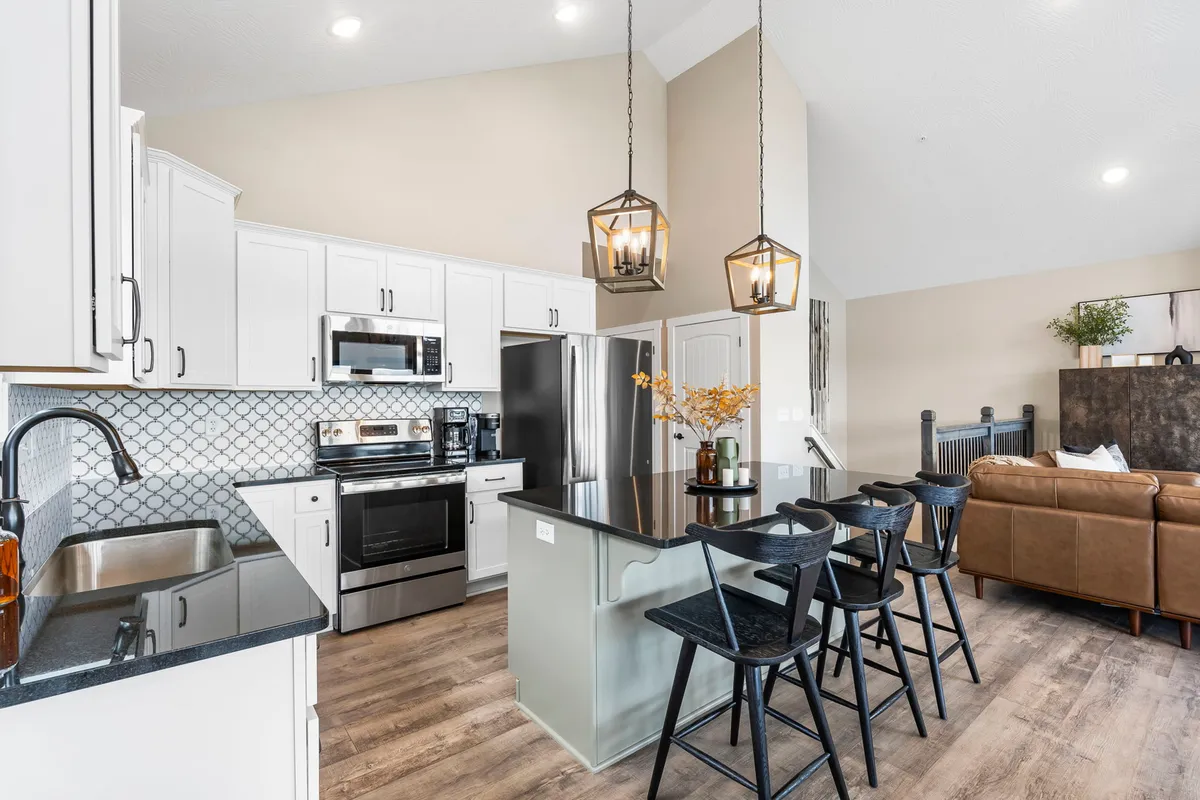 This image highlights a stylish kitchen island with seating beneath elegant pendant lights, complemented by modern appliances and a decorative vase of fresh flowers. The open design suggests a seamless flow between the kitchen and adjacent social spaces.
