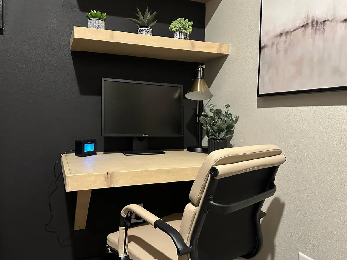A serene, productive office nook with a wooden desk, computer monitor, desk lamp, shelving with plants, and a comfortable chair. Ample natural light pours in, creating an inspiring environment for work or study.