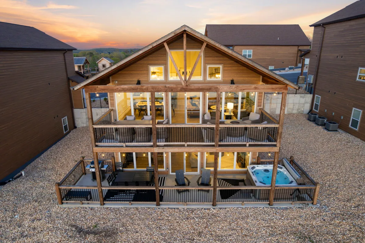 This exterior image showcases a wooden deck with outdoor seating and a hot tub, all overlooking the lake. Large windows from the interior connect visually to the deck, suggesting easy indoor-outdoor flow. The sunset view adds a sense of tranquility and luxury.